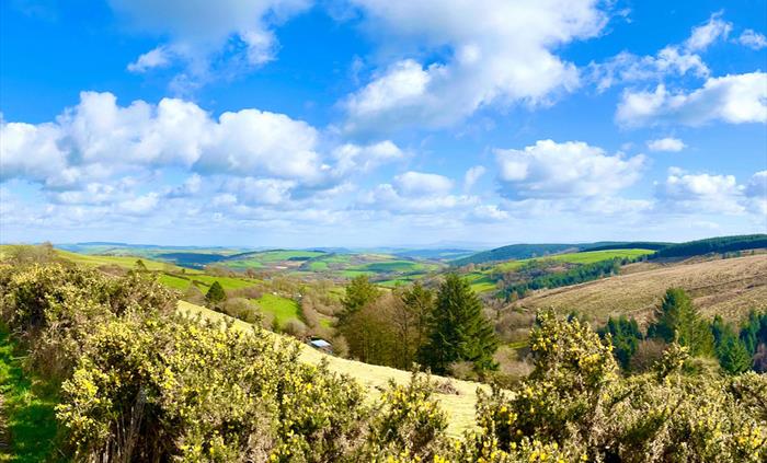 A view over the surrounding Carmarthenshire countryside with blue skies, a patchwork of fields and the Brecon Beacons in the distance.